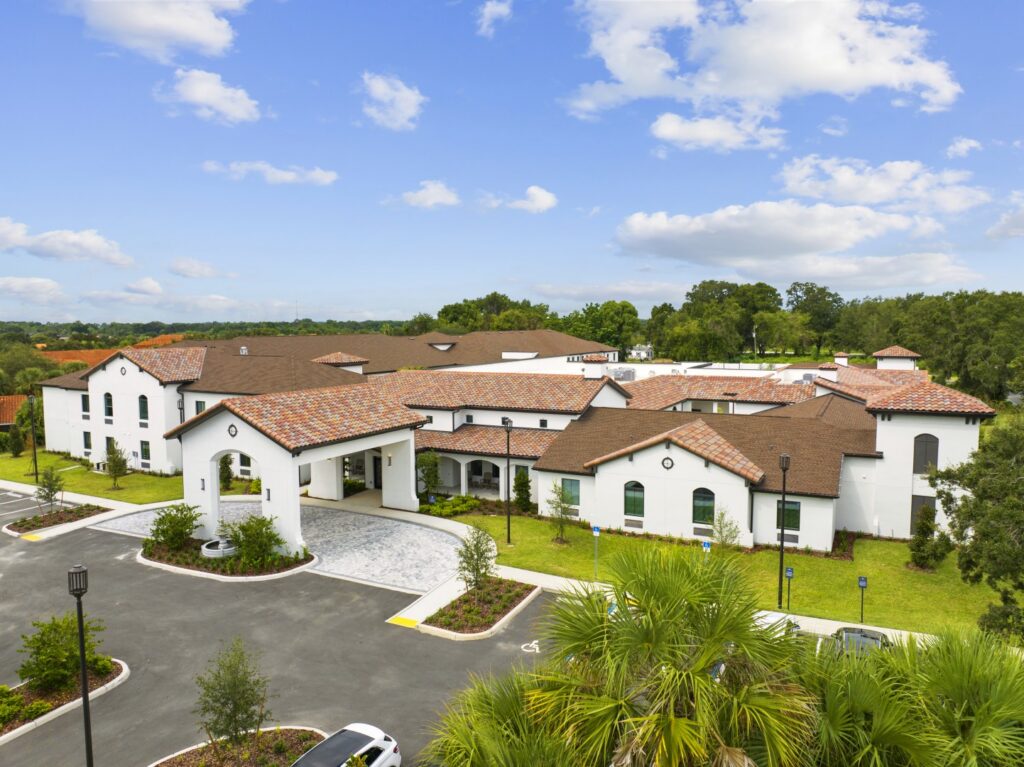 Mediteranean style Senior Living Building white walls and spanish tile roof, under blue skies with porte cochere