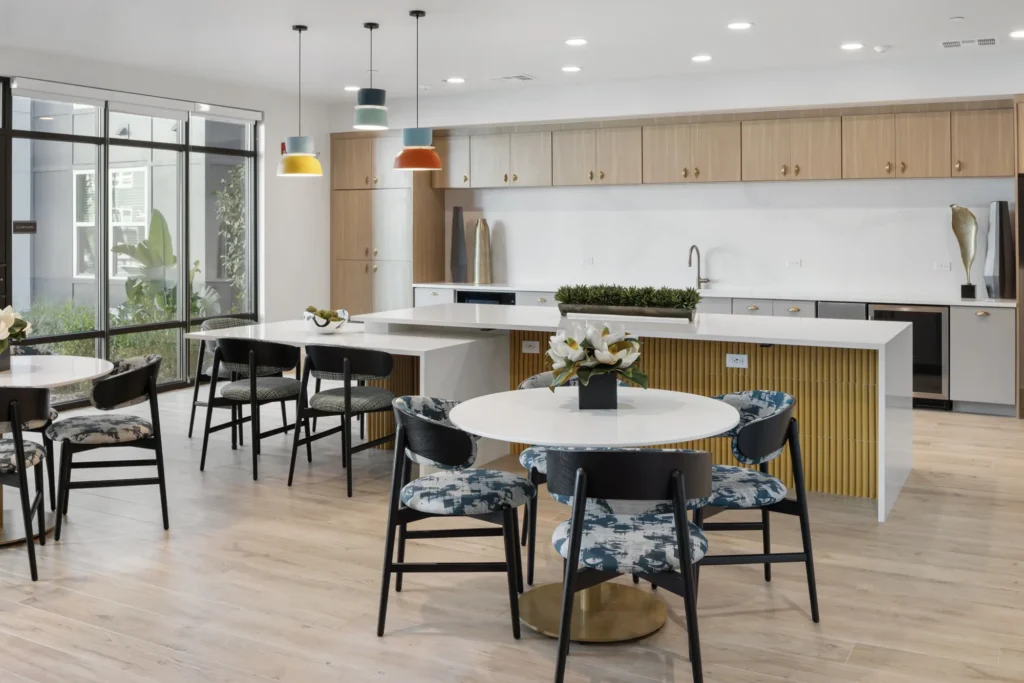 A common area at The Aston at Uptown with a large kitchen, cabinets, and four-top tables.
