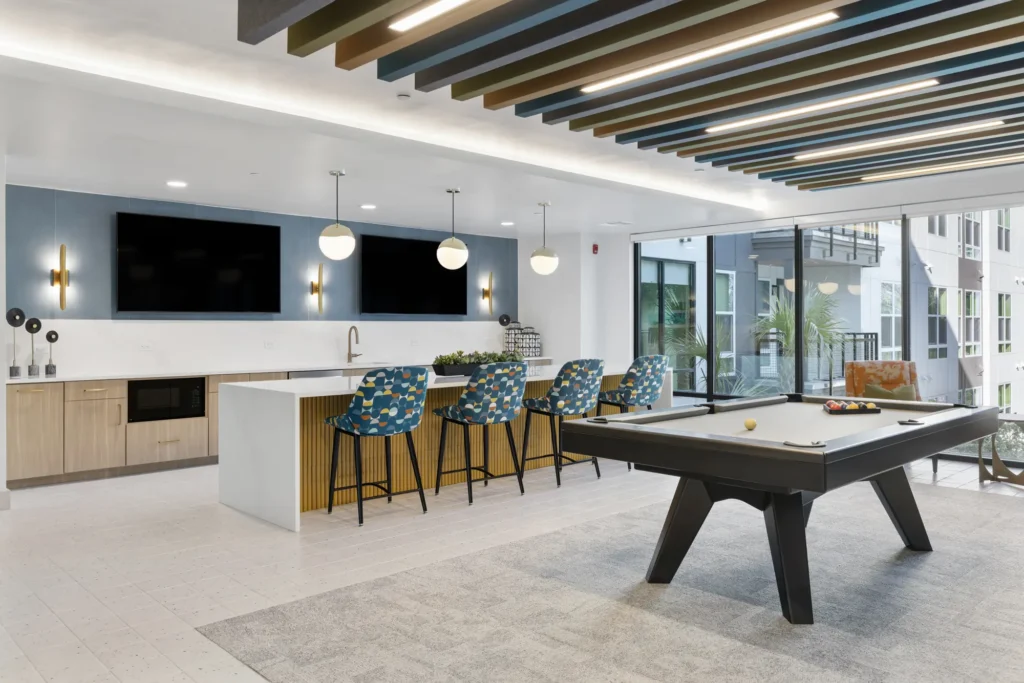 A common area at The Aston at Uptown with a bar, kitchen area, TVs, and a pool table.