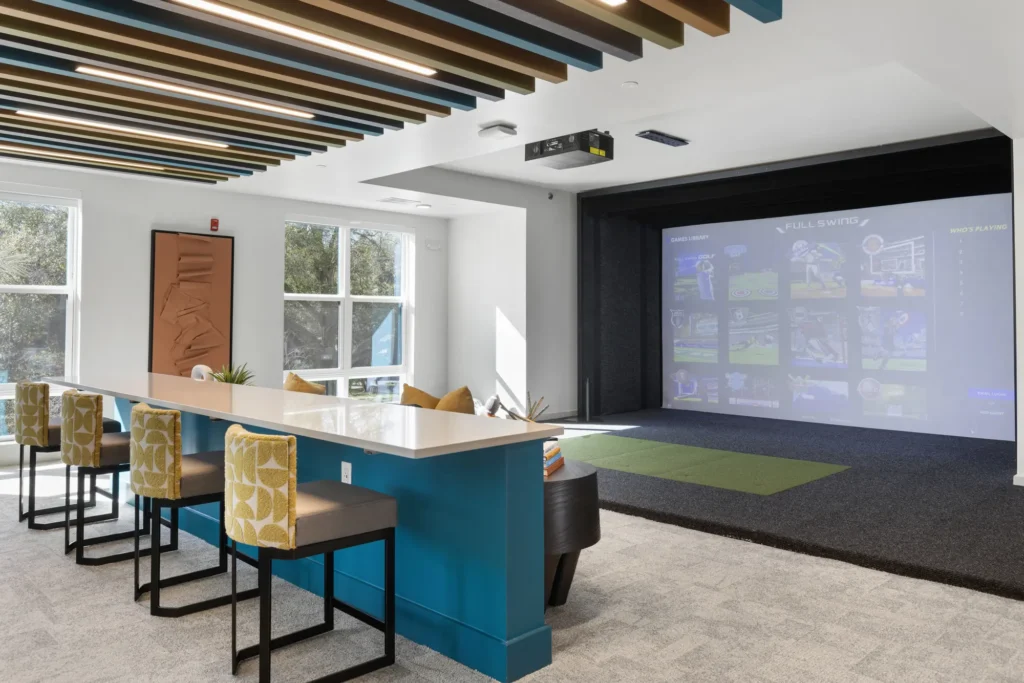 A common area at the Aston at Uptown with a bar, stools, digital projector, and a large screen