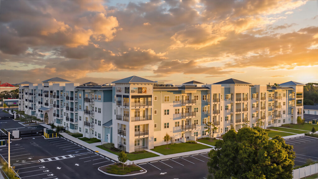 Lantower Bayside's four-story building in light blue and white siding at sunset, with black-railed balconies, warmly lit windows and the name "LANTOWER BAYSIDE" mounted on a white central tower